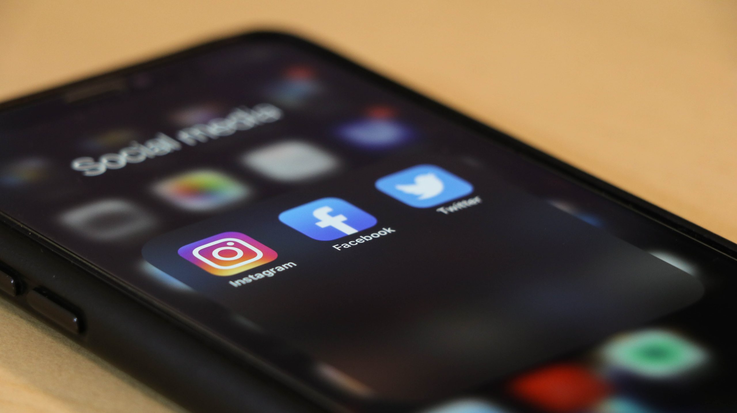 A black smartphone has several social media apps showing inside a folder. The phone is on a light colored desk.